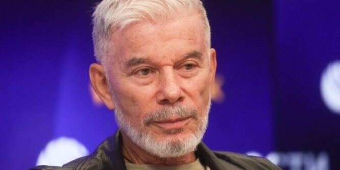 74-летний Олег Газманов, с полностью седой бородой и без футболки, позирует рядом со своей 56-летней супругой, одетой в боди с прозрачными вставками.